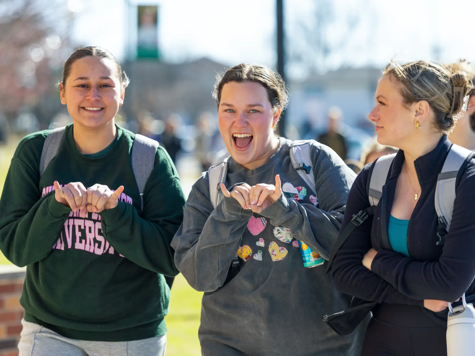 Female OBU students looking into camera giving bison horns sign.