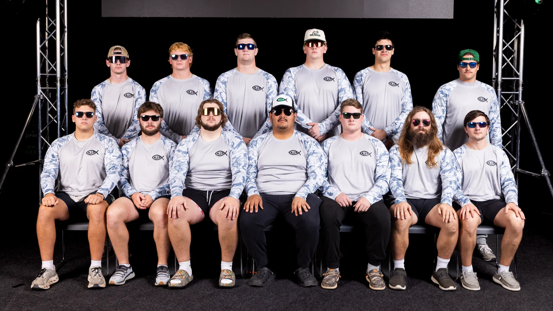 Twelve members of the Bass Fishing Club pose together in two rows, wearing matching blue-camo long-sleeve fishing shirts and sunglasses.
